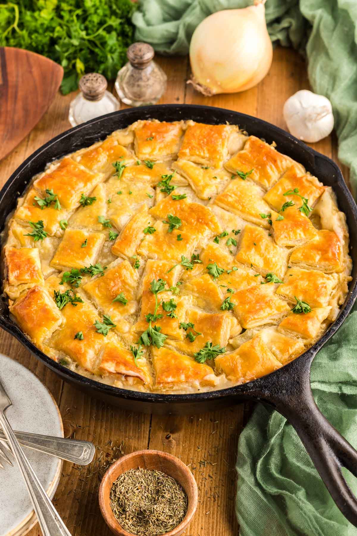 A cast-iron skillet filled with chicken pot pie that is topped with a puff pastry crust and garnished with parsley.