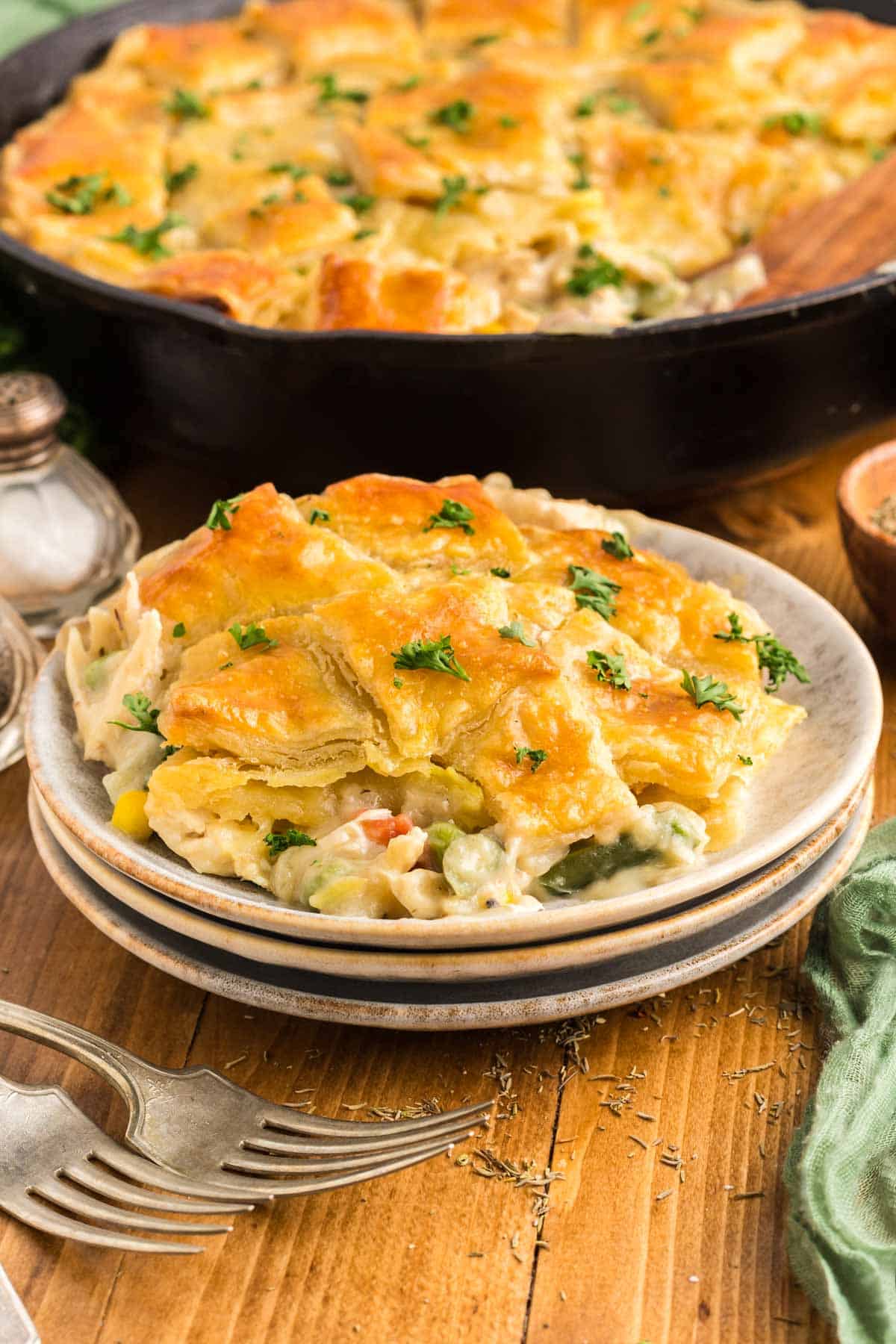 Chicken pot pie, scooped onto a serving plate with the pot pie in the cast-iron skillet in the background.