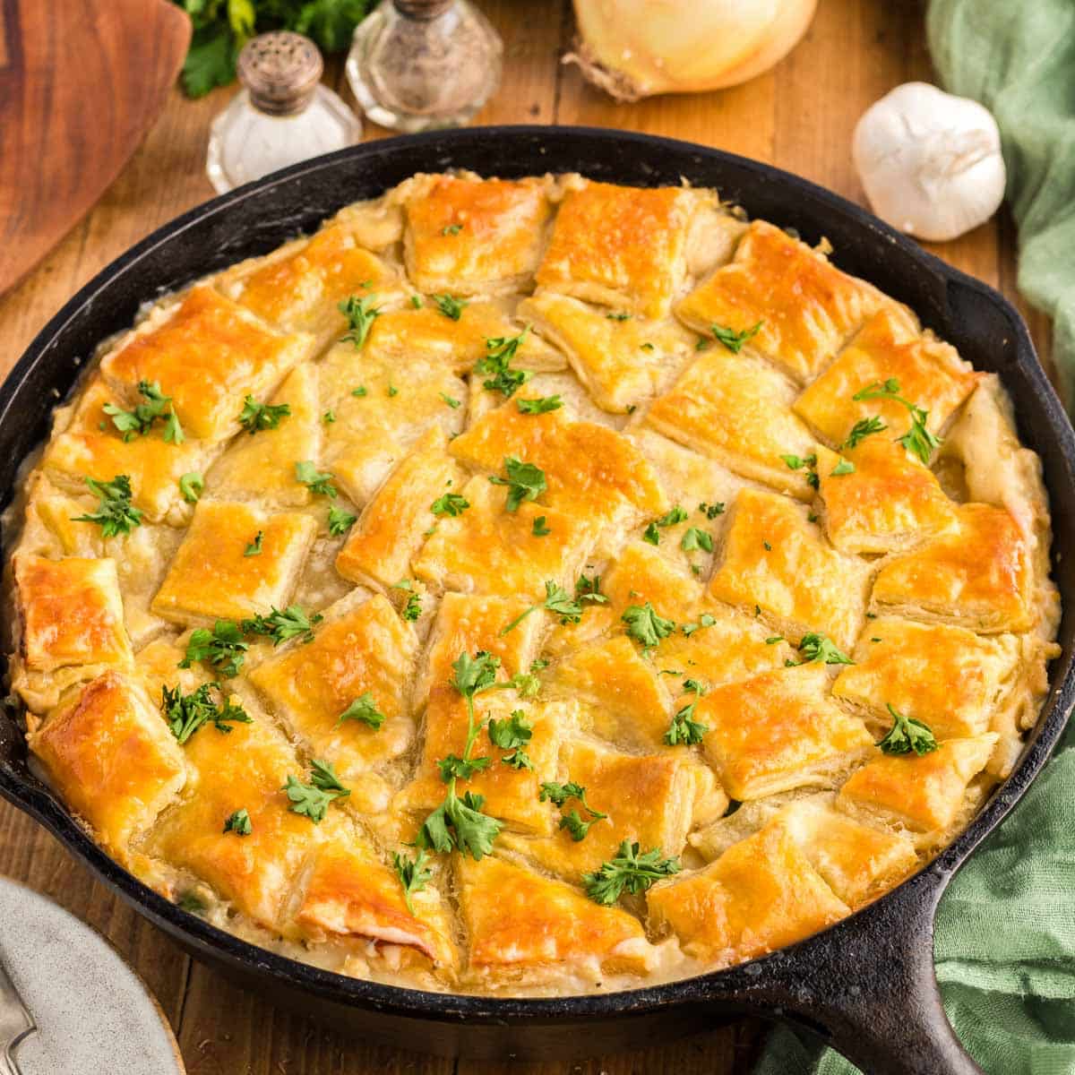 A cast-iron skillet filled with chicken pot pie that is topped with a puff pastry crust and garnished with parsley.