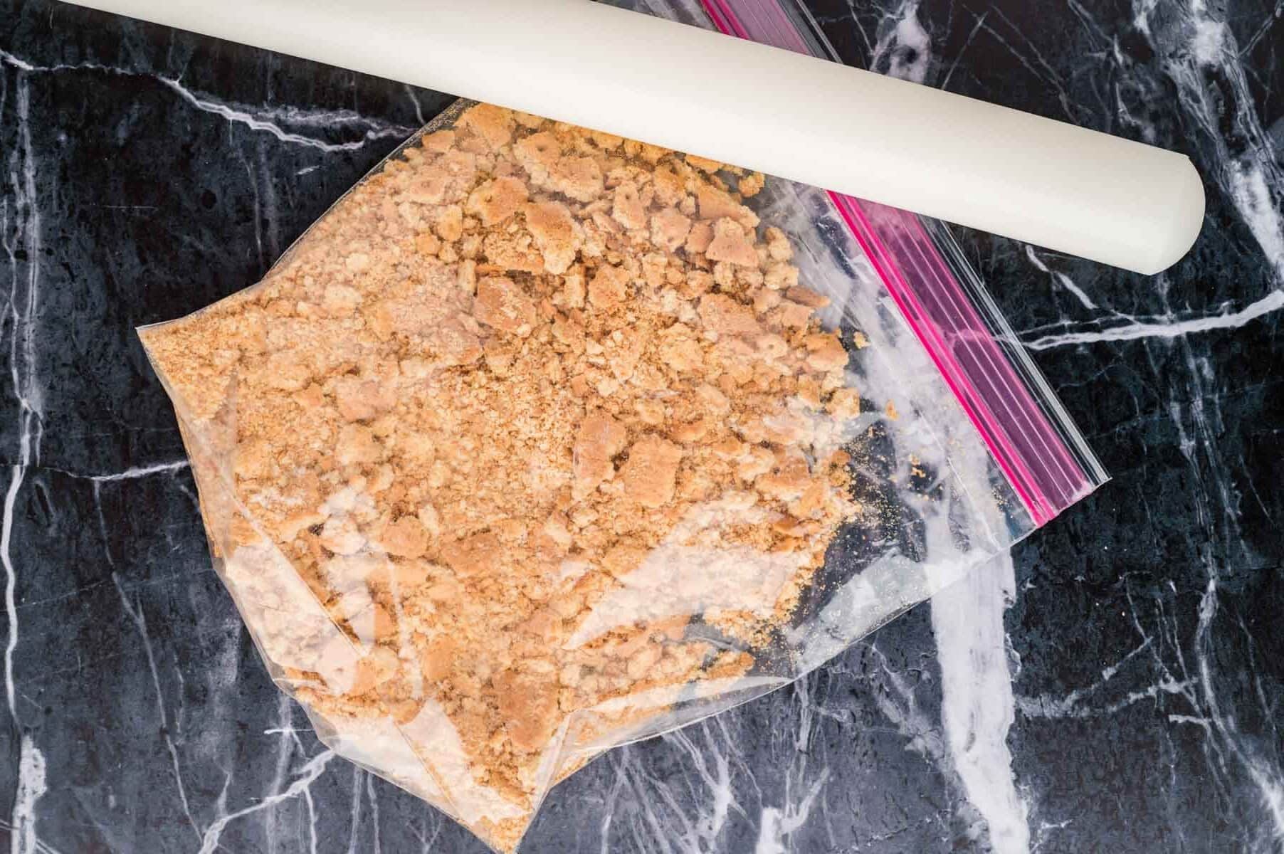 A rolling pin smashing graham crackers in a Ziploc bag.