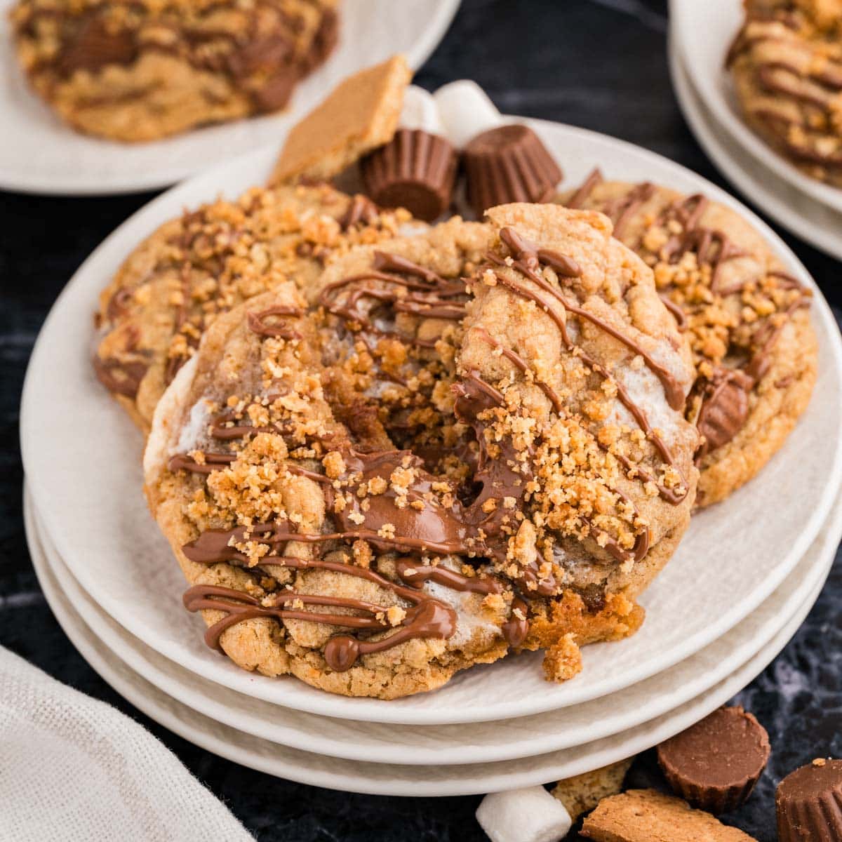 Peanut butter s'mores cookies, drizzled with Reese's chocolate drizzle, and graham cracker topping on a white plate.