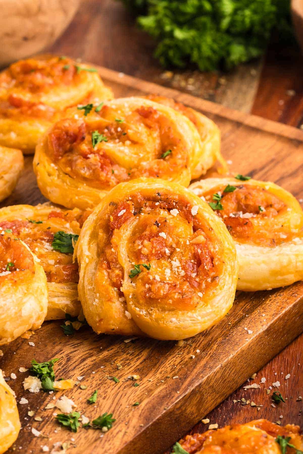 Pepperoni pinwheels on a wooden board sprinkled with parsley and Parmesan cheese.