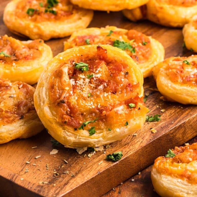 Pepperoni pinwheels on a wooden board sprinkled with parsley and Parmesan cheese.