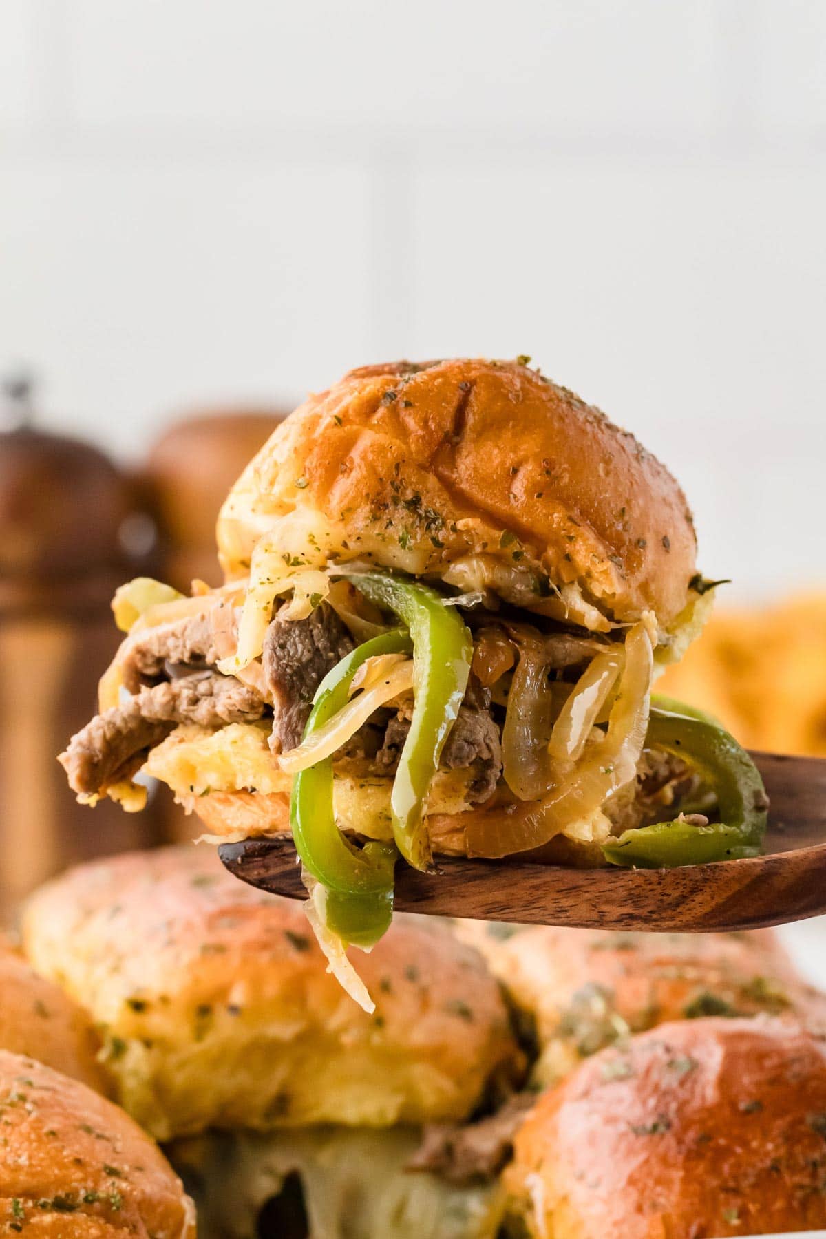 A wooden spatula picking up a Philly cheesesteak slider from the baking dish.