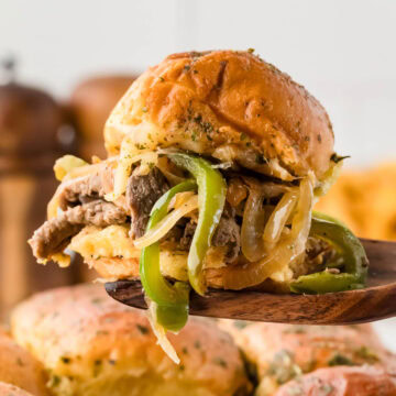 A wooden spatula picking up a Philly cheesesteak slider from the baking dish.