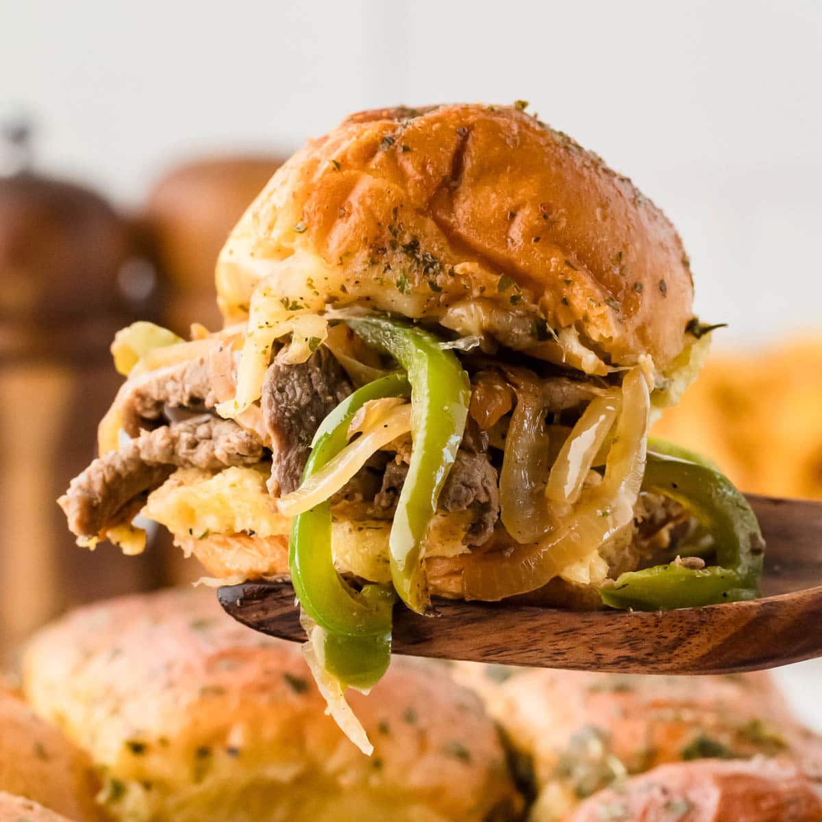 A wooden spatula picking up a Philly cheesesteak slider from the baking dish.