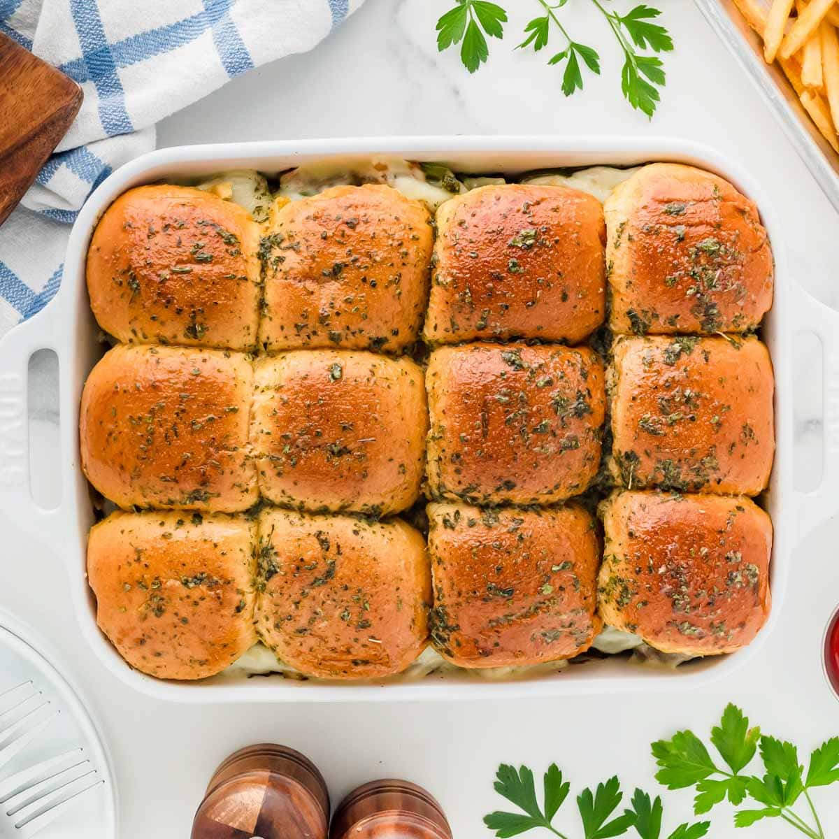 A white baking dish full a Philly cheesesteak sliders.