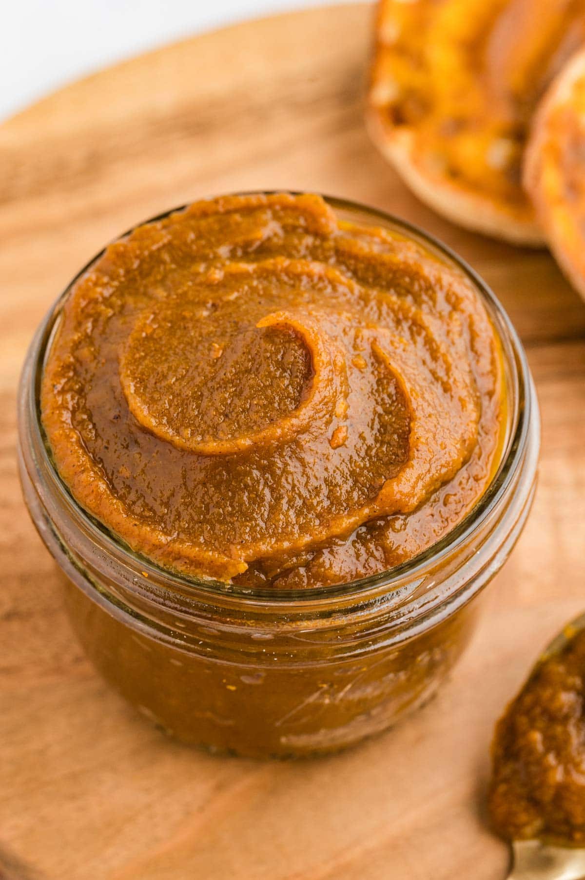 A jar of pumpkin butter with a pretty swirl on top set on a wooden board.