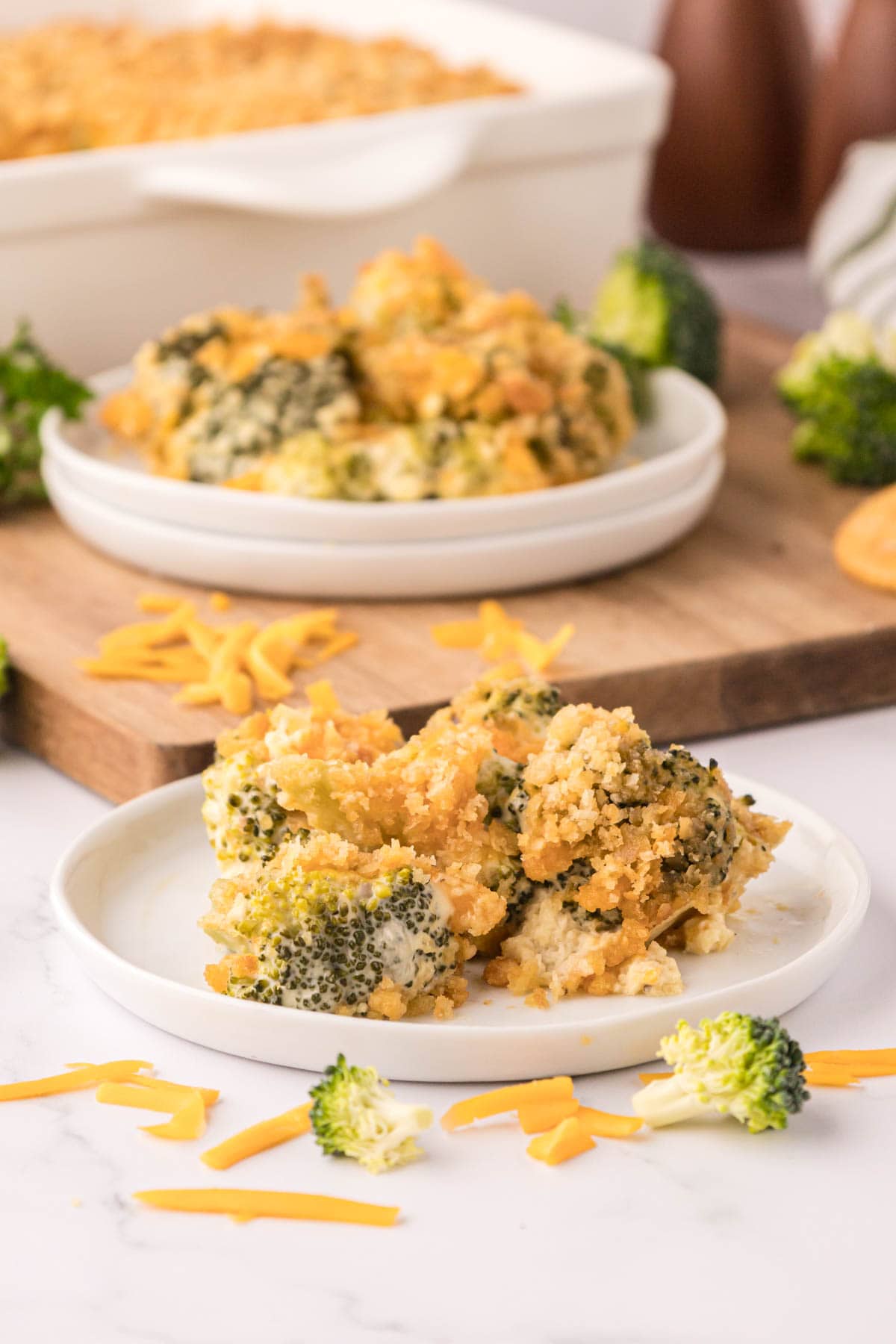 A white plate with broccoli casserole on it with the casserole dish in the background.