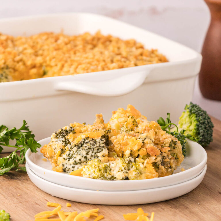 A white plate with broccoli casserole on it with the casserole dish in the background.