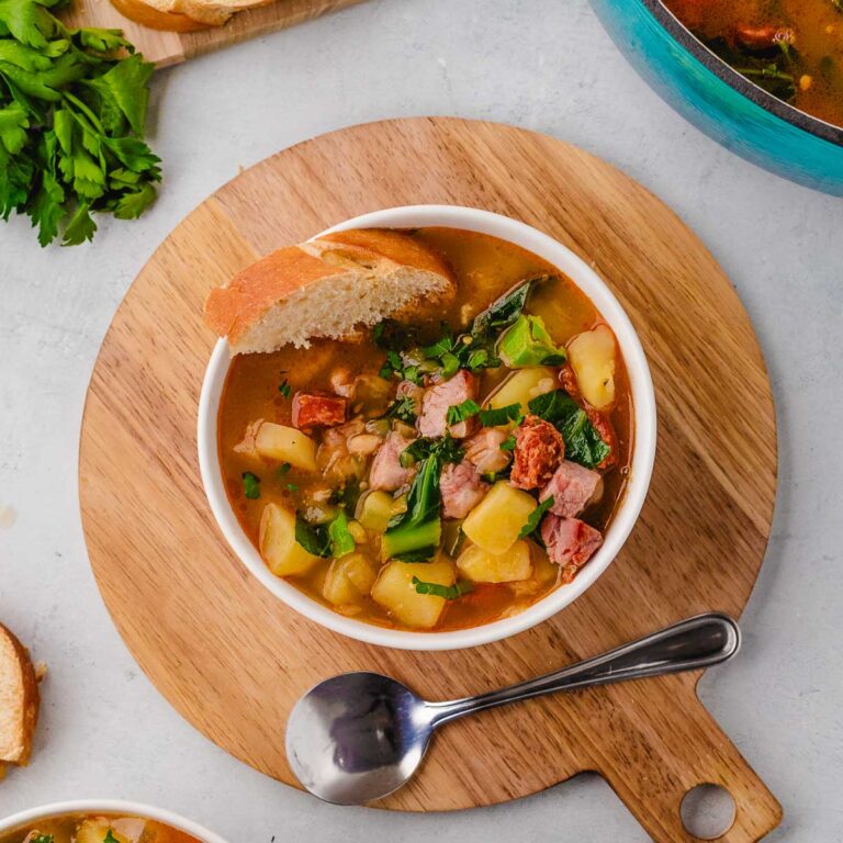 A bowl of Caldo Gallago (Galetian broth) soup on a wooden tray with a spoon.