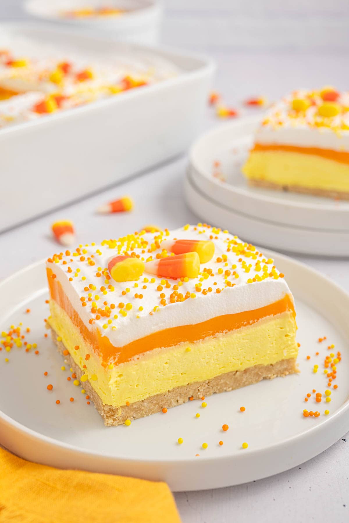 Slice of candy corn lush dessert served on a plate with another slice in the background. 