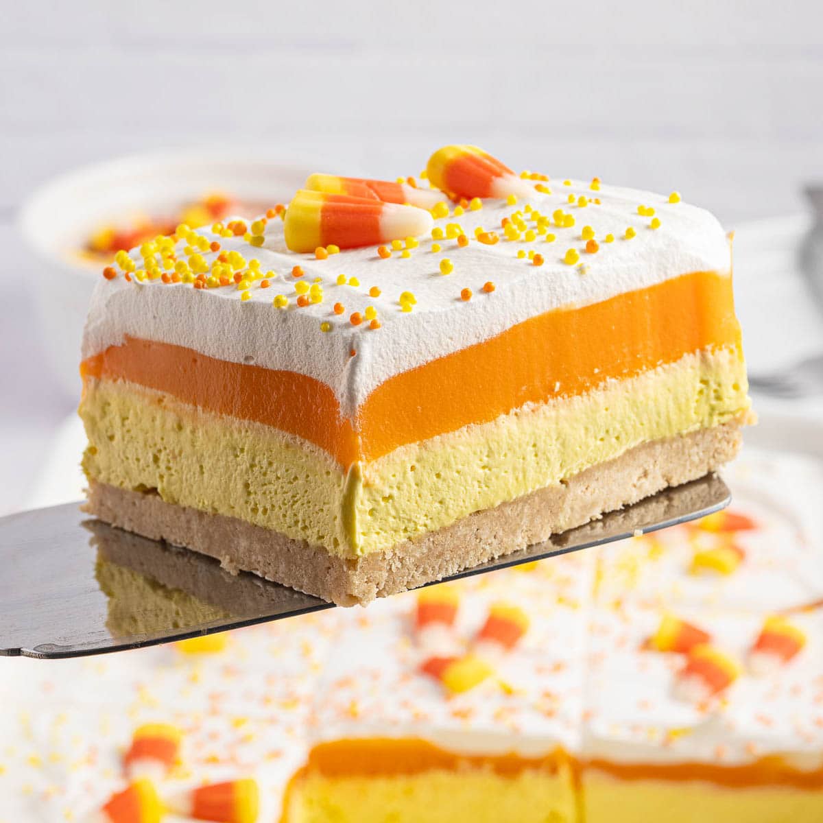 Slice of candy corn lush dessert served on a plate with another slice in the background.