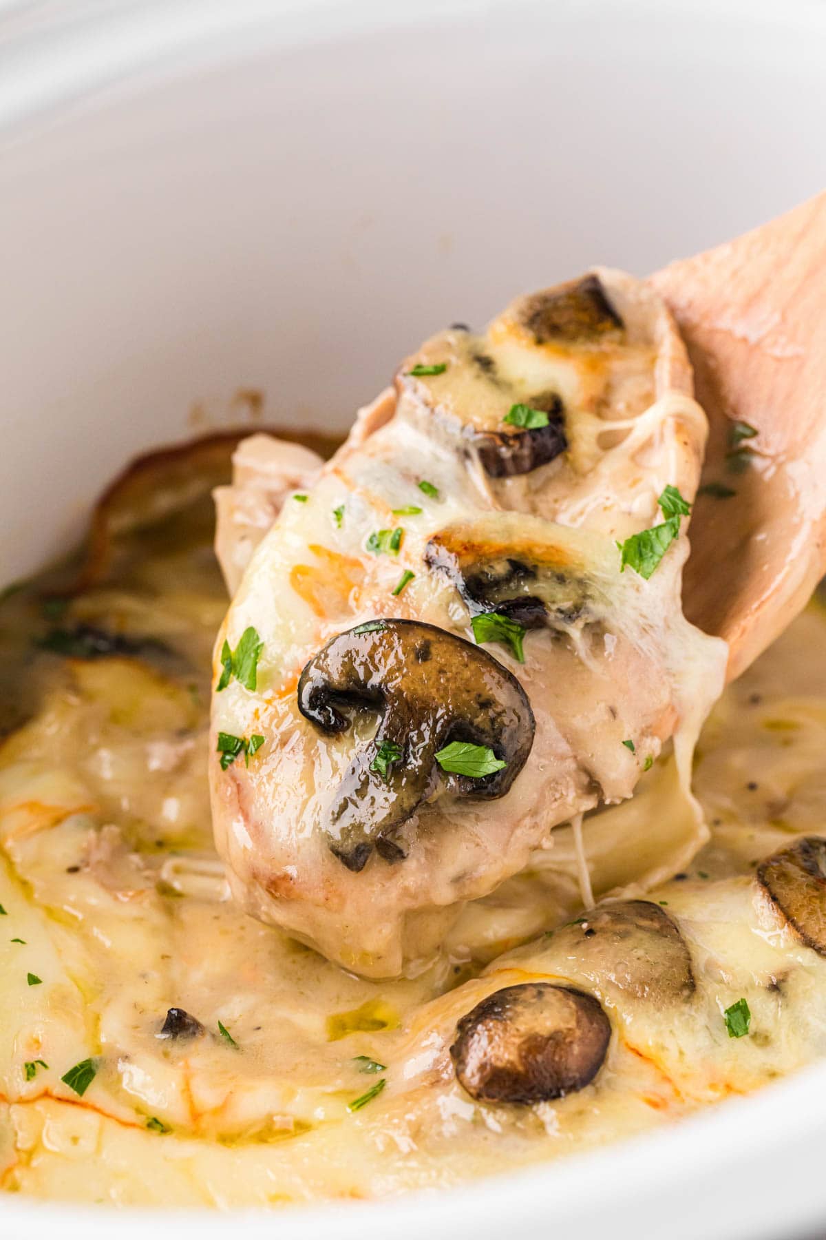 A wooden spoon scooping out a serving of chicken from crock pot.