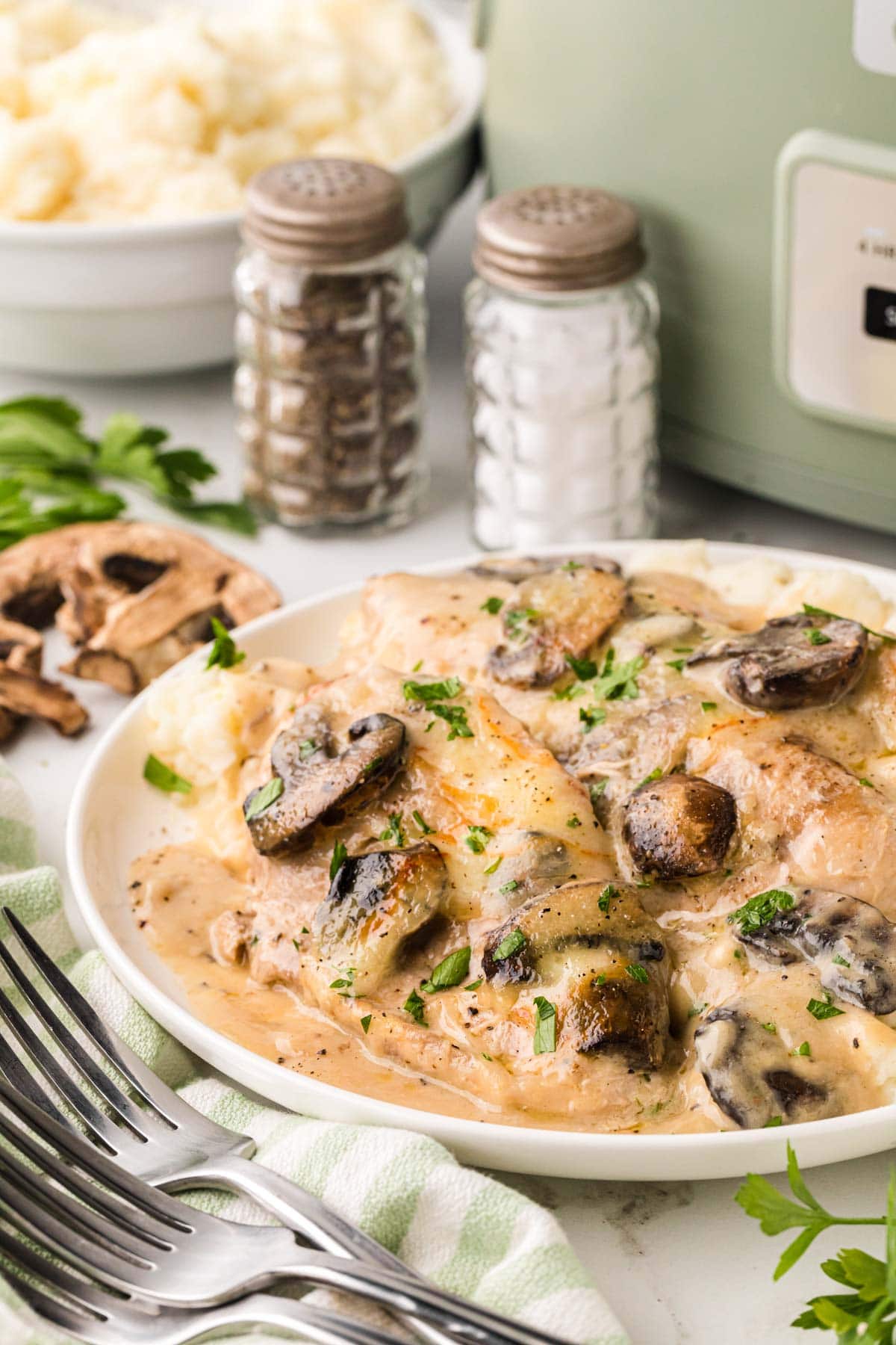 A white plate filled with creamy mushroom chicken plated over mashed potatoes.