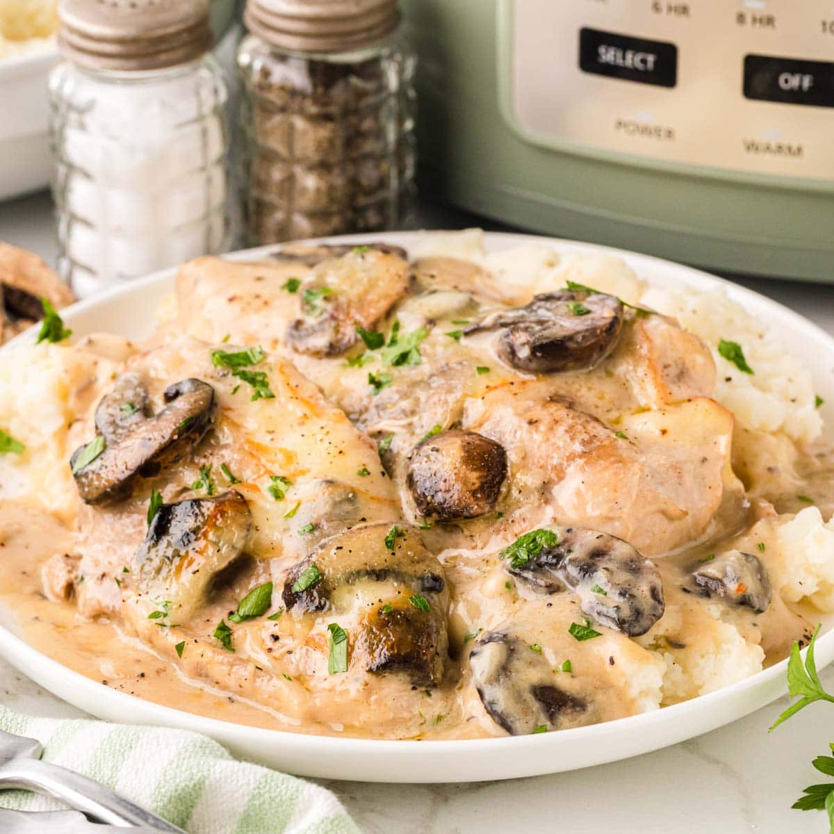 A white plate filled with creamy cheesy mushroom chicken plated over mashed potatoes.