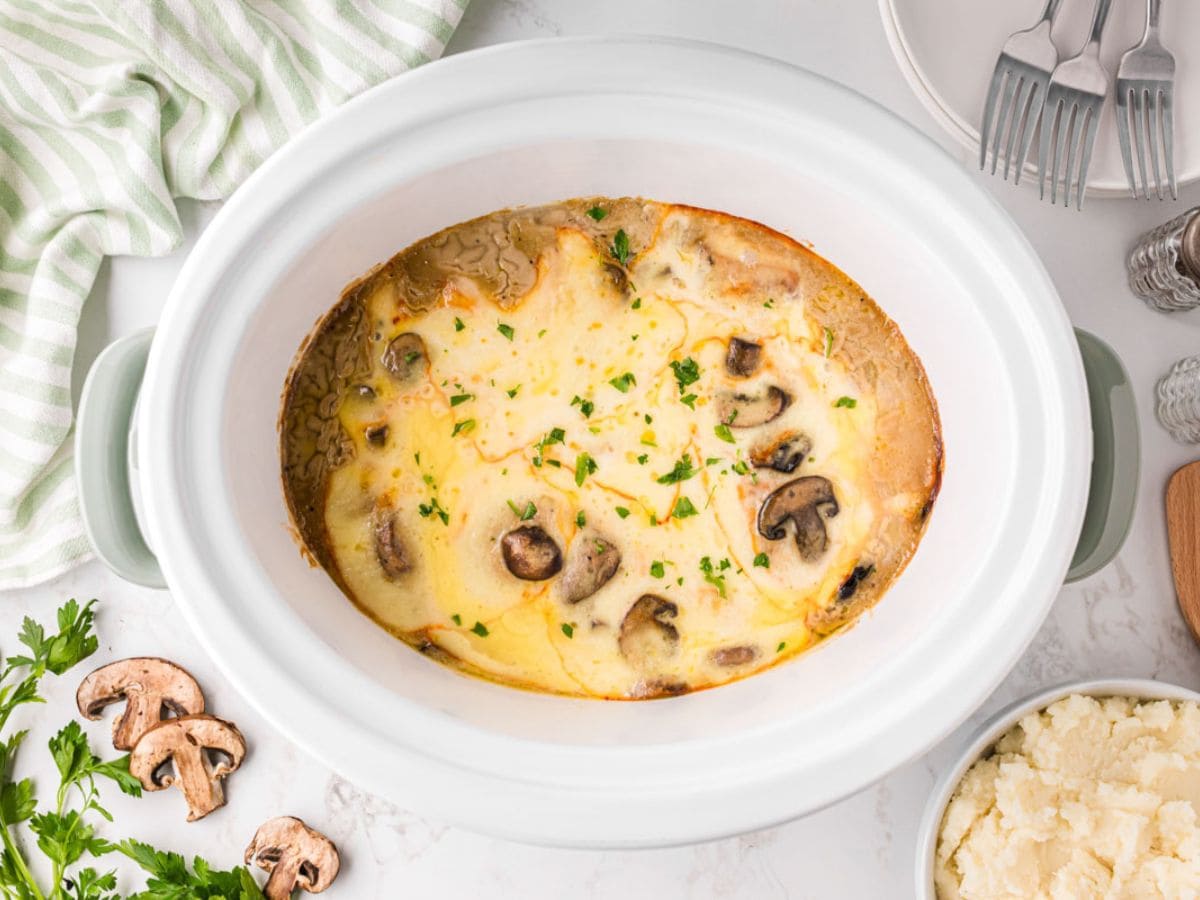 Slow cooker, mushroom chicken topped with melted cheese after being cooked.