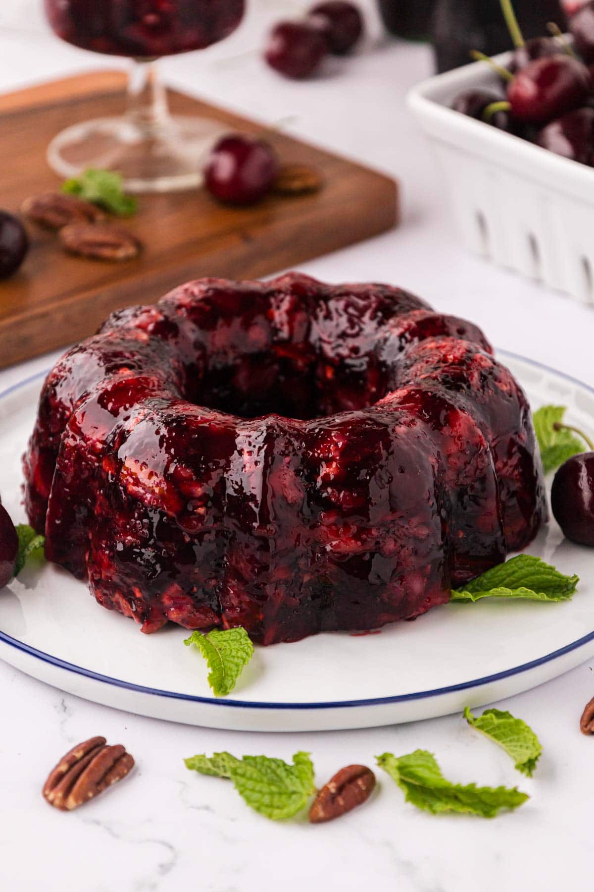 A cherry Coke Jell-O salad that was formed in a Jell-O bowl displayed on a beautiful white plate with leaves.