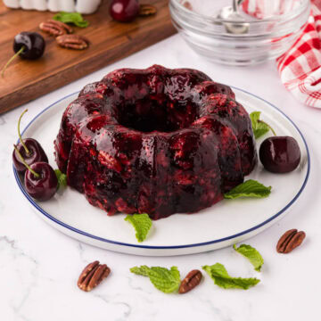 A cherry Coke Jell-O salad that was formed in a Jell-O bowl displayed on a beautiful white plate with leaves.