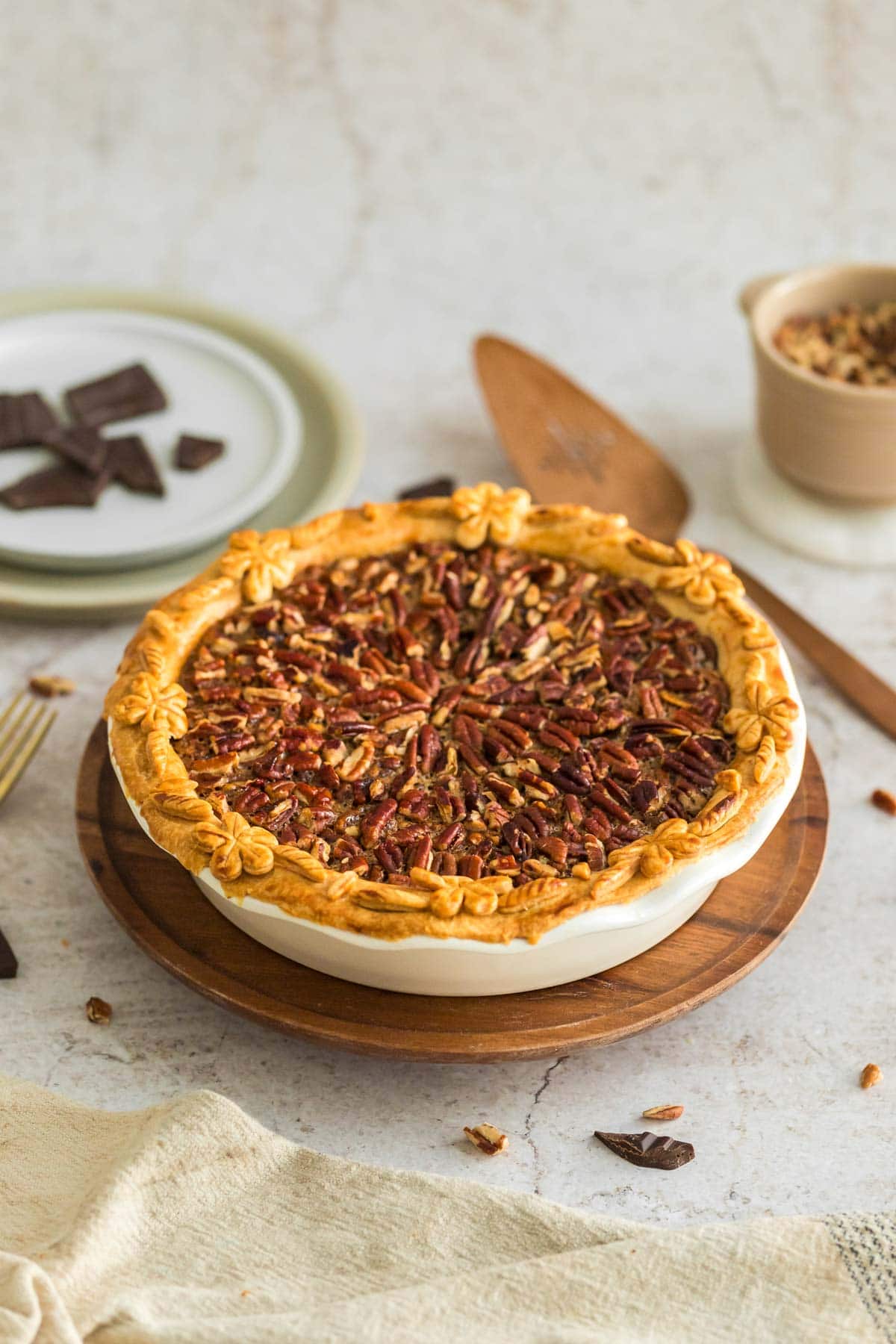 A chocolate pecan pie set on a wooden tray with a pie server in the background.