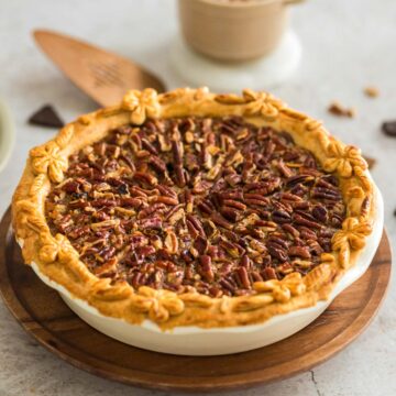 A chocolate pecan pie set on a wooden tray with a pie server in the background.