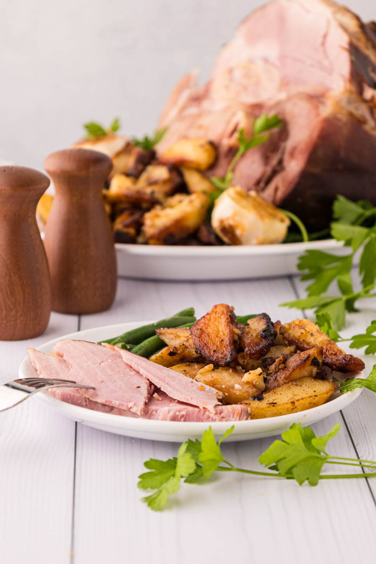 A white plate with slices of country ham, potatoes and green beans.