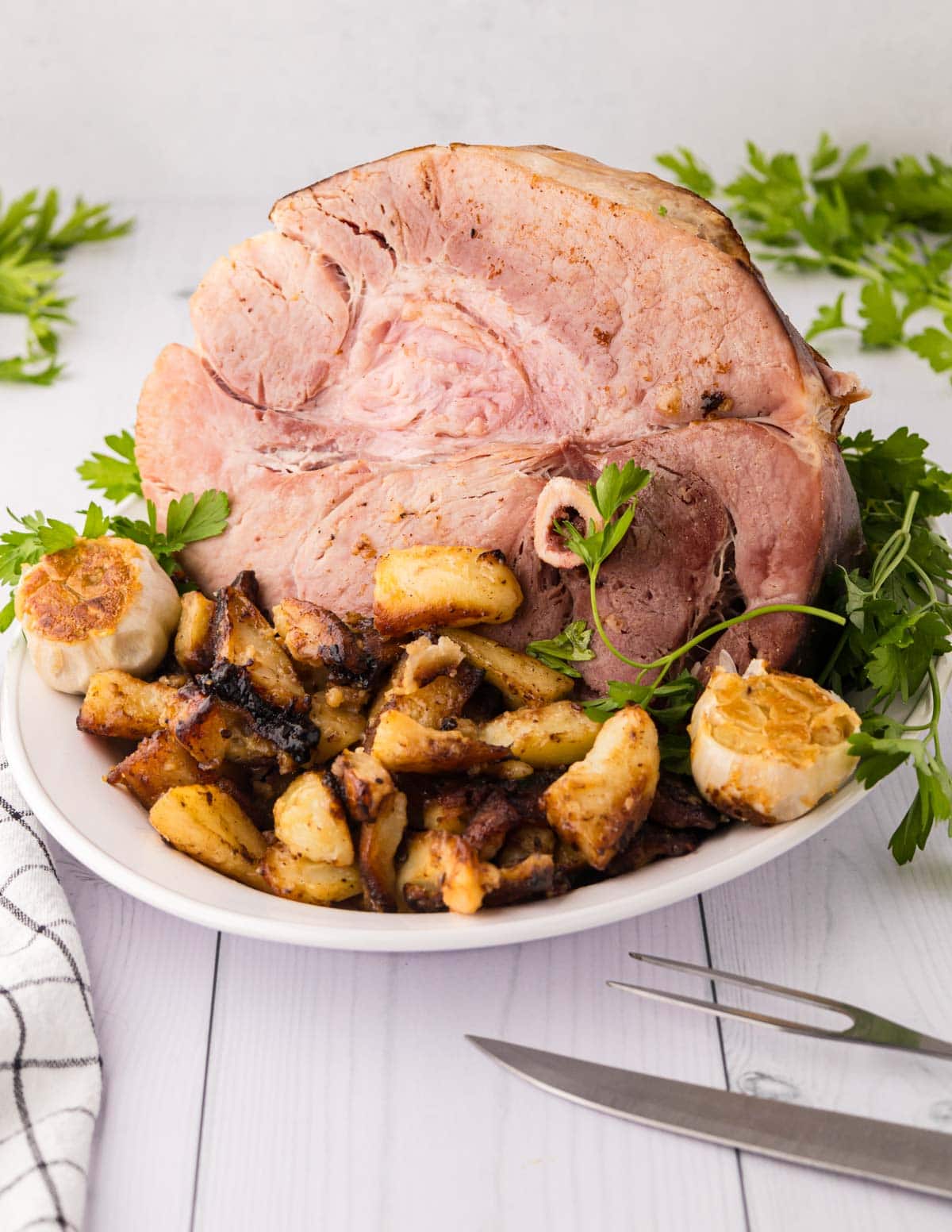 A white serving plate with a half country ham and skillet browned potatoes.