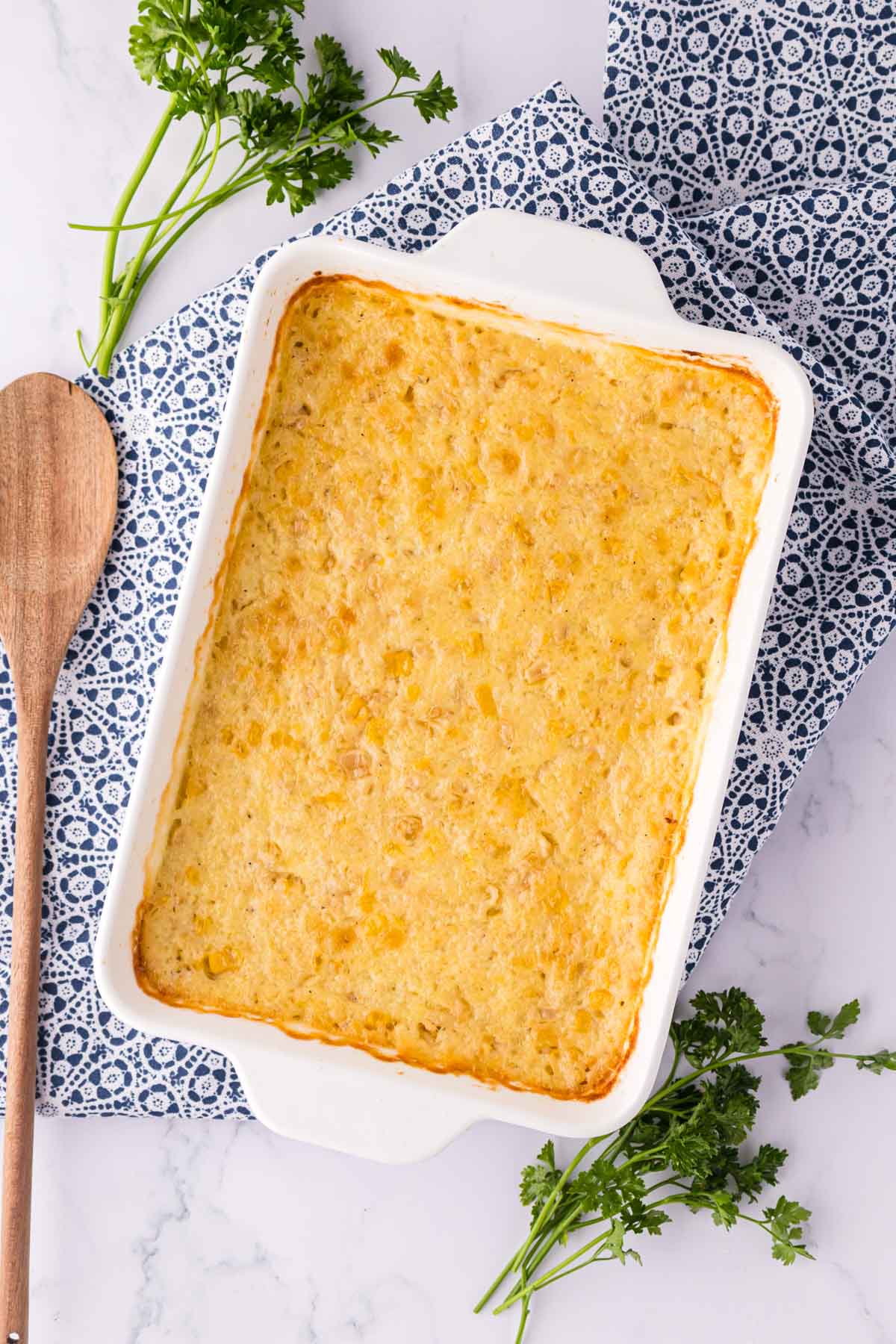 A white casserole dish filled with baked creamed corn casserole.