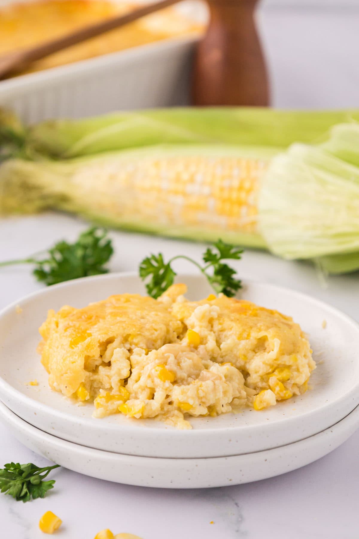 A white plate with a serving of cream corn casserole, garnished with parsley.