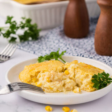 A white plate with a serving of cream corn casserole, garnished with parsley.