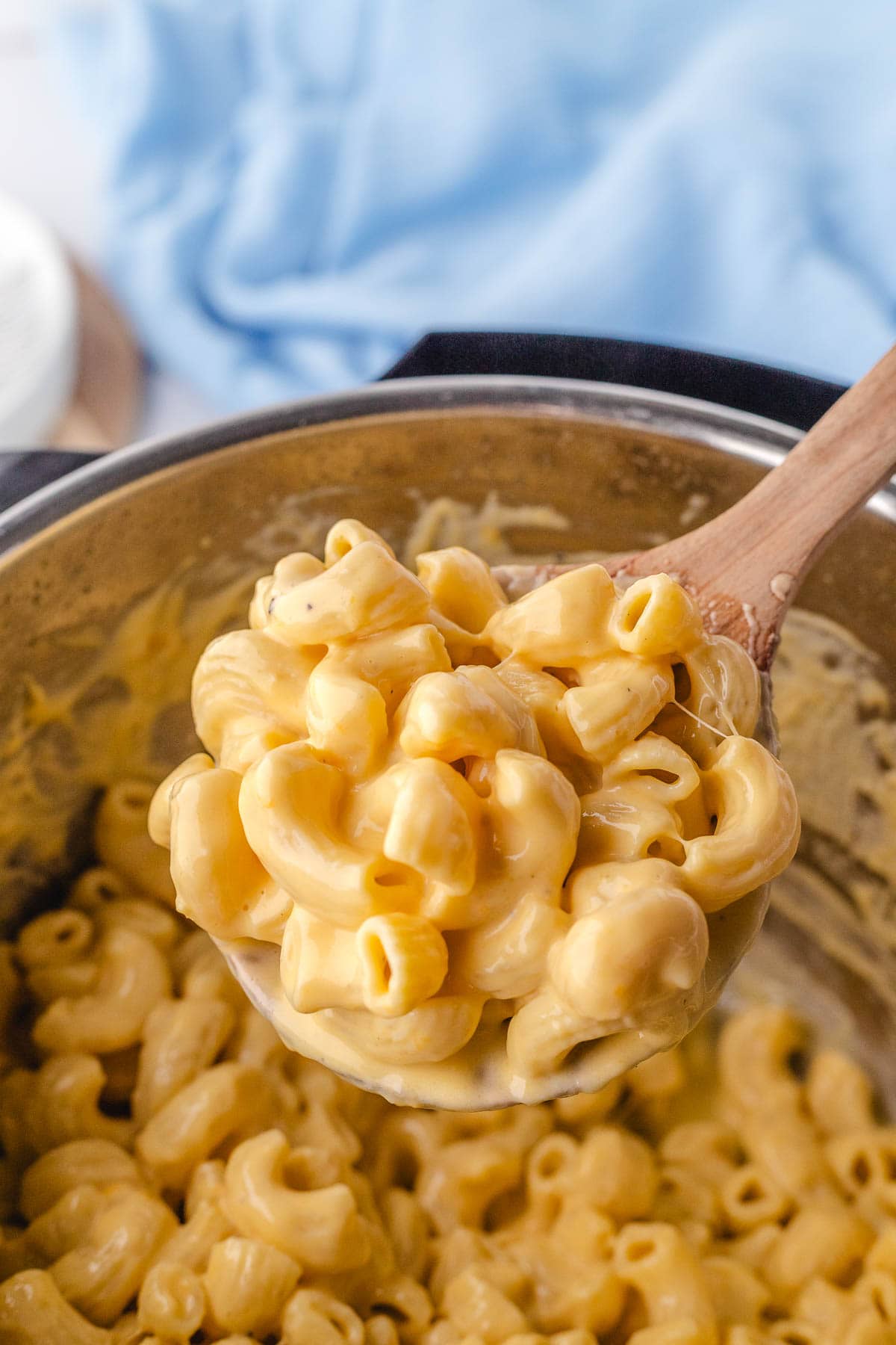 An instant filled with creamy mac and cheese with a wooden spoon removing a serving.