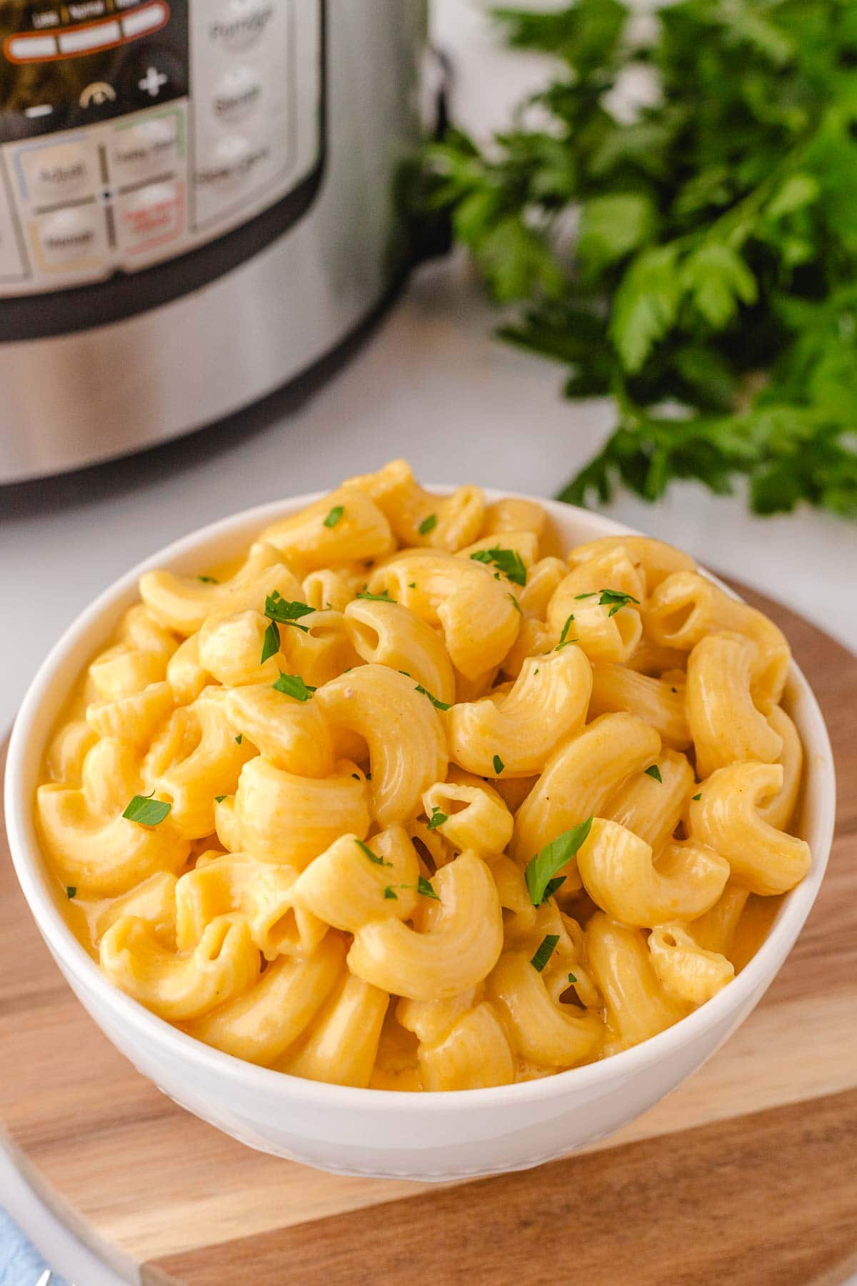 A white bowl filled with cream instant pot macaroni and cheese with the instant pot in the background.