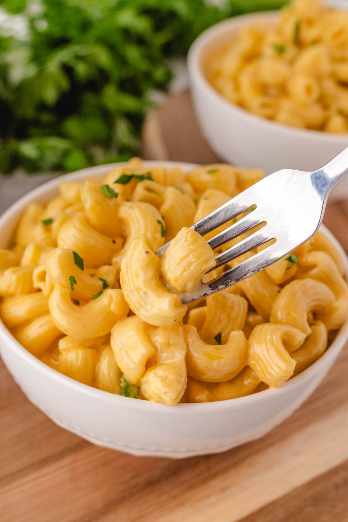 A silver fork picking up a bite of macaroni and cheese from a white bowl.