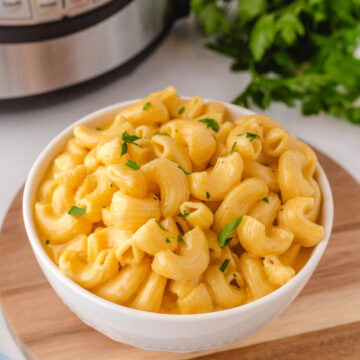 A white bowl filled with cream instant pot mac and cheese with the instant pot in the background.