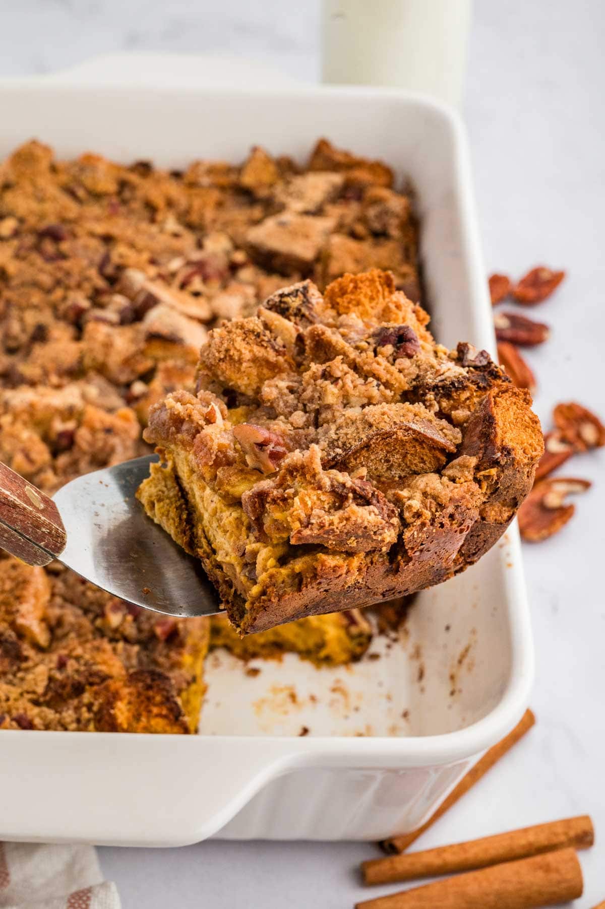 Spatula holding a corner piece of the pumpkin French toast casserole with the baking dish below it.