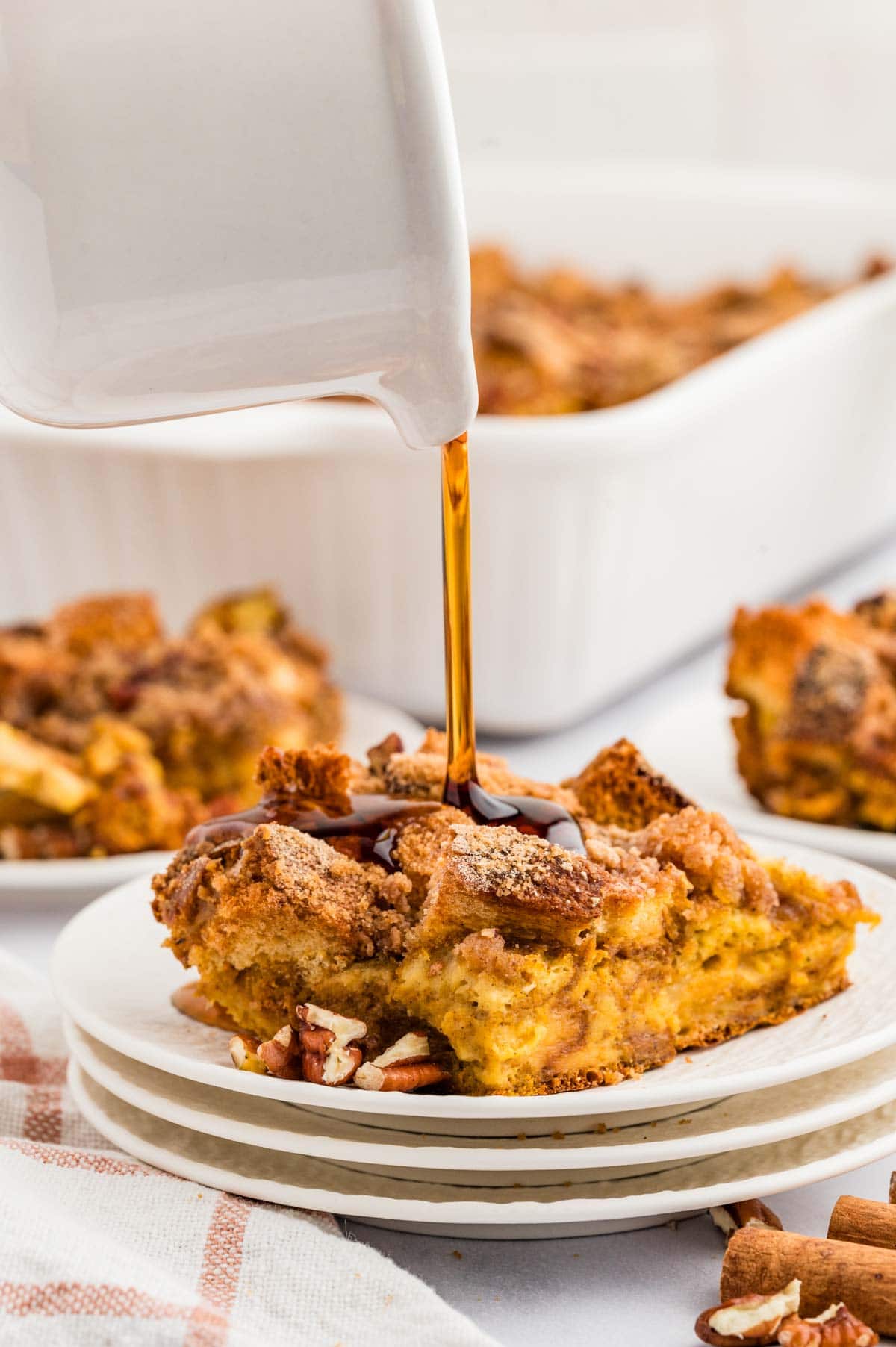 Pouring maple syrup onto a piece of pumpkin French toast casserole on a white plate.