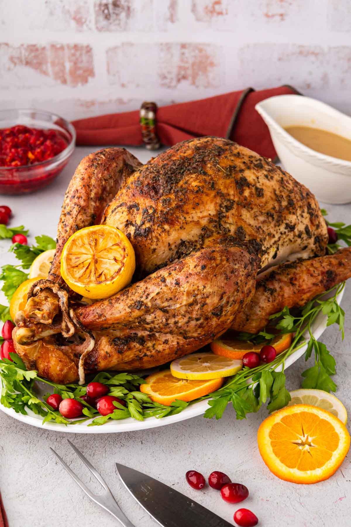 A seasoned roasted turkey on a white platter garnished with parsley, cranberries, oranges and lemons.