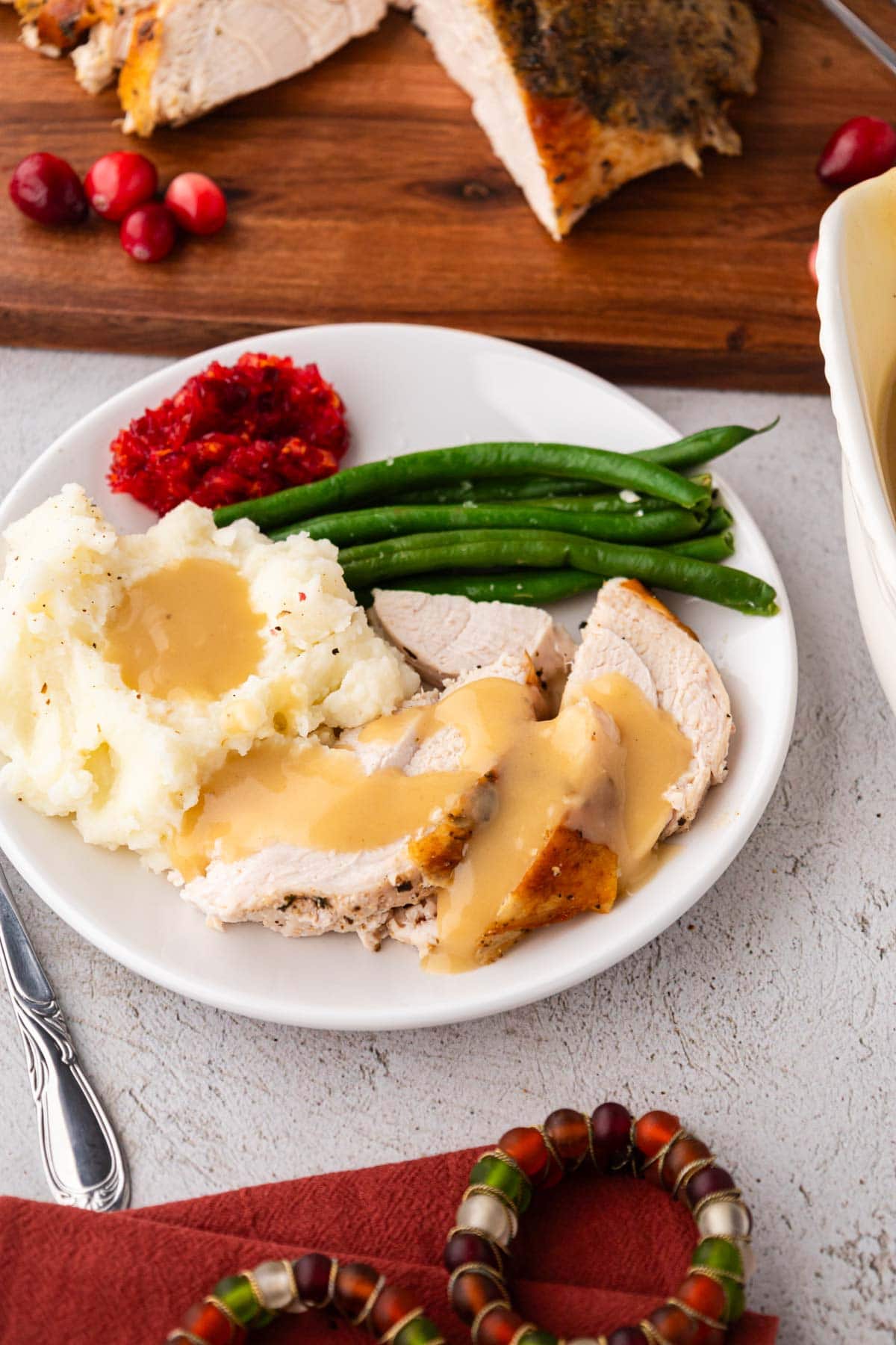 A white plate with sliced turkey topped with gravy along with mashed potatoes and green beans.