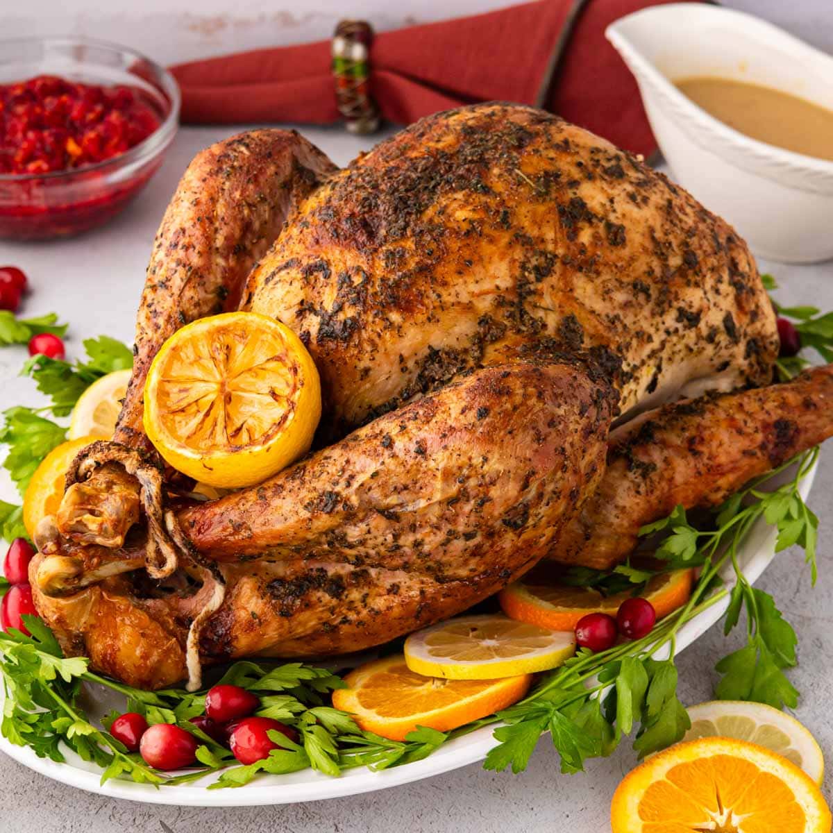 A seasoned roasted turkey on a white platter garnished with parsley, cranberries, oranges and lemons.