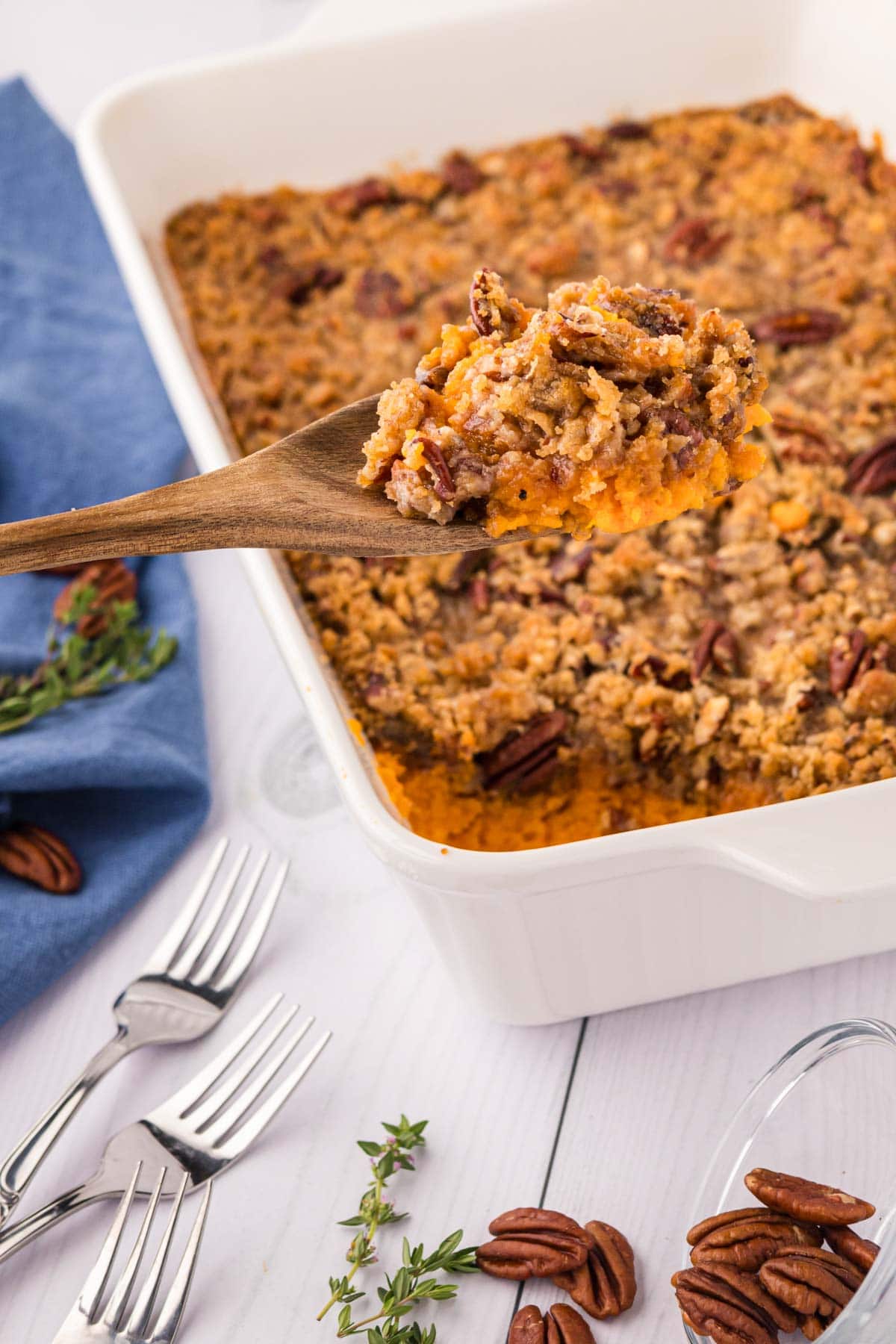 A wooden spoon removing a scoop of sweet potato soufflé from a white casserole dish.