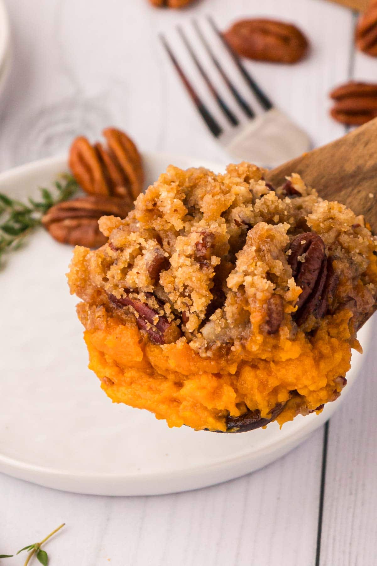 A wooden spoon, scooping, sweet potato casserole onto a white plate.