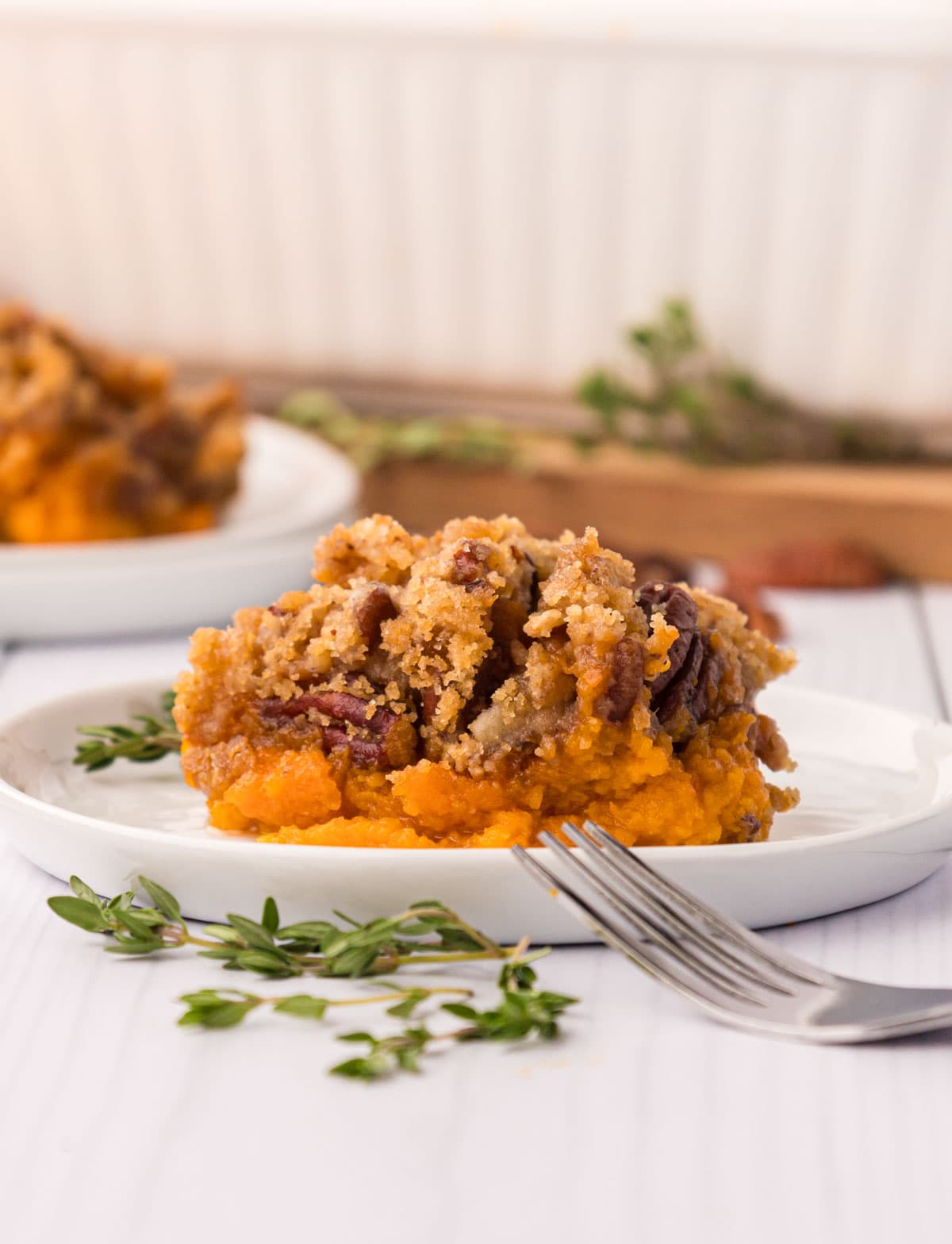 A white plate with a scoop of sweet potato casserole with pecan crumb topping.