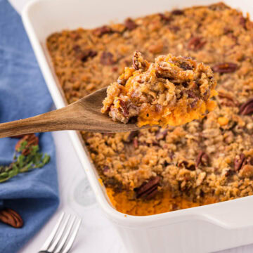 A wooden spoon removing a scoop of sweet potato soufflé from a white casserole dish.