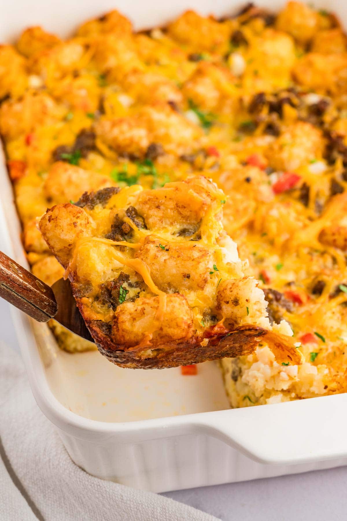 Spatula picking up a corner piece of the tater tot breakfast casserole from the baking dish.