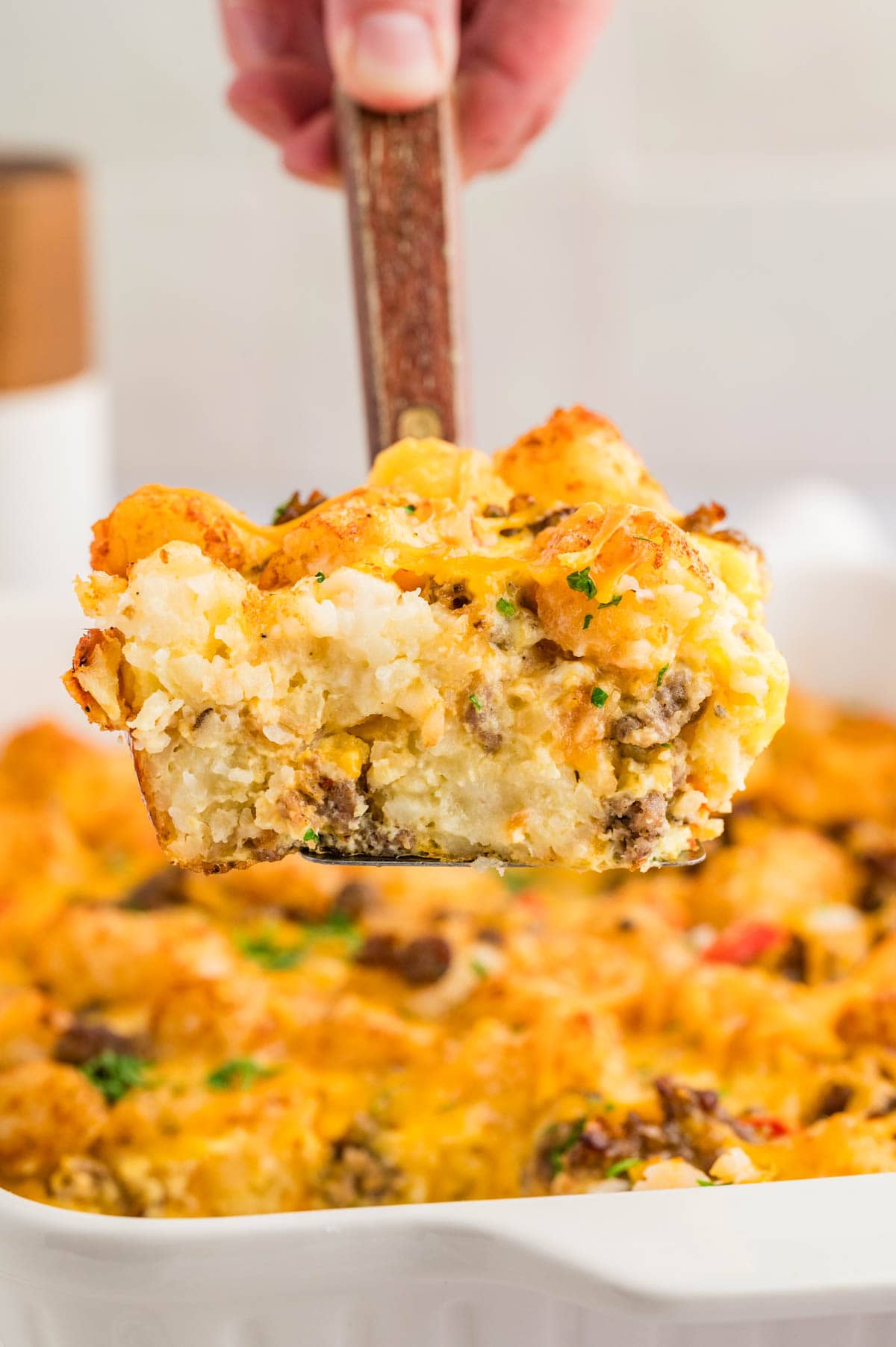 Spatula holding a piece of tater tot breakfast casserole with the whole casserole underneath it.