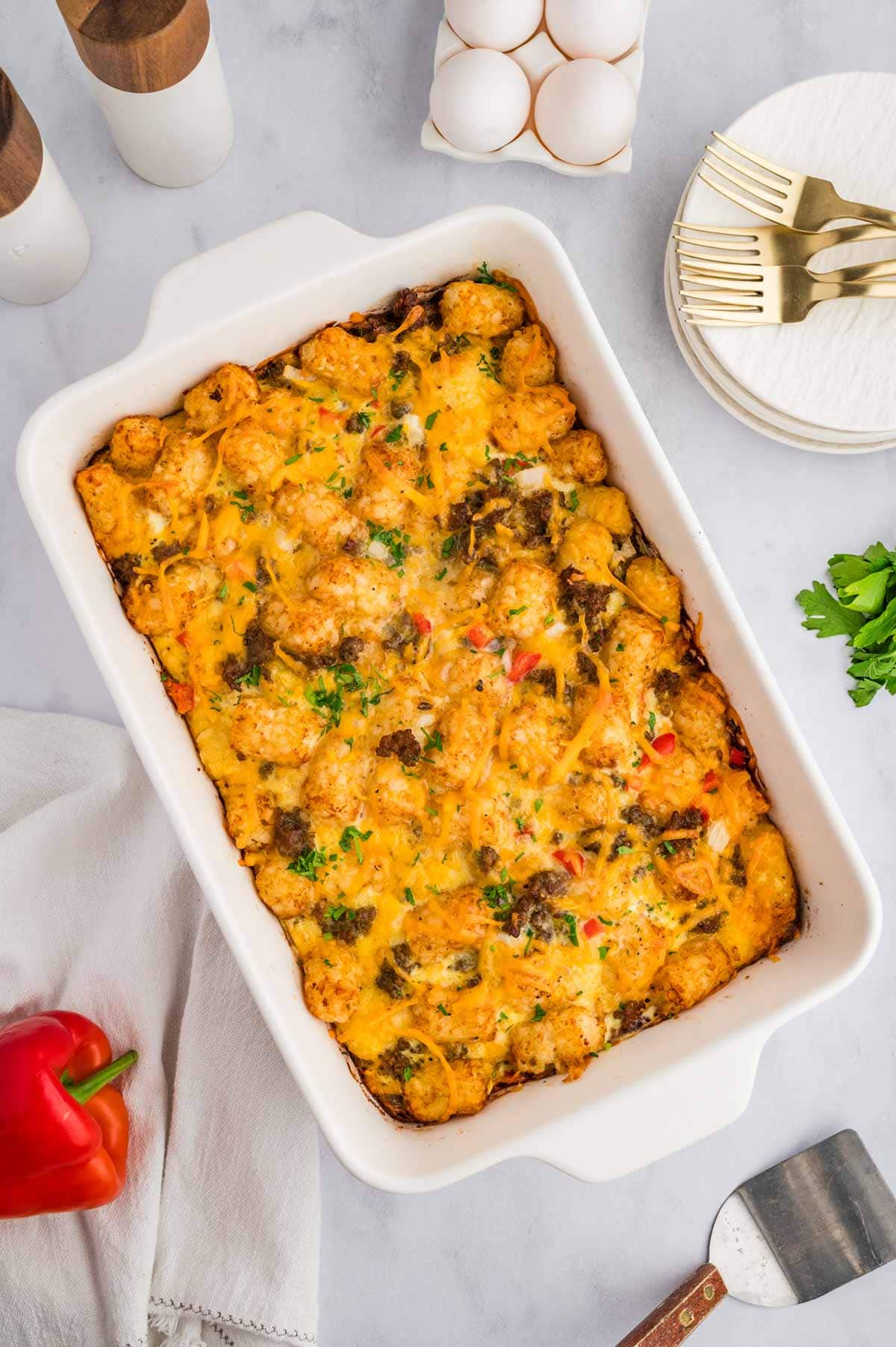 Overhead shot of tater tot breakfast casserole on a counter with eggs next to plates and forks.