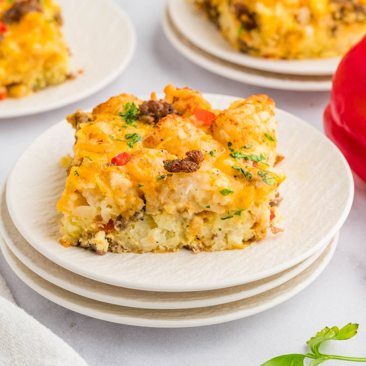 Slice of tater tot breakfast casserole on a stack of white plates.