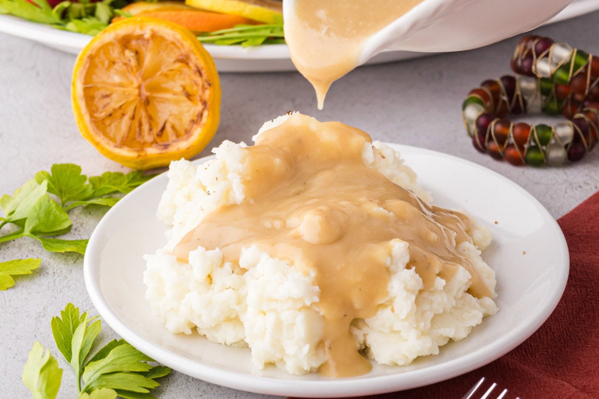 Pouring turkey gravy on top of a plate of mashed potatoes.