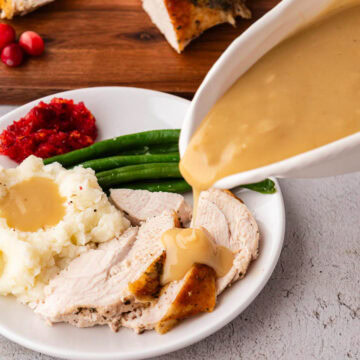 Pouring homemade gravy on top of a plate of sliced turkey with mashed potatoes and green beans.