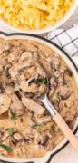 A saucepan with beef stroganoff with a bowl of noodles in the background.